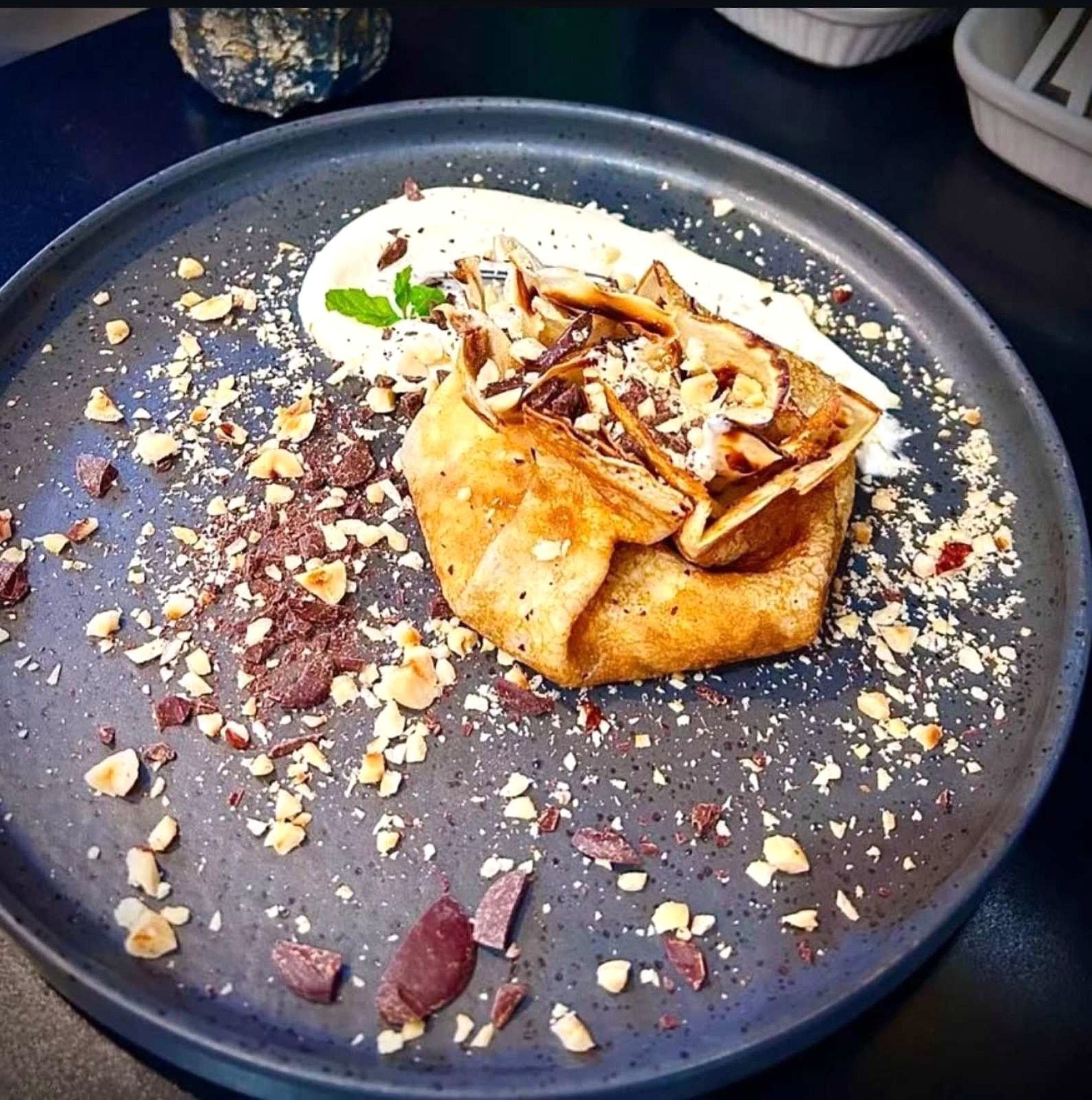 Une assiette de dessert avec une crêpe, de la crème fouettée et des copeaux de chocolat.