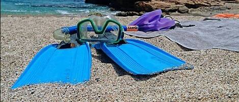 A pebbled beach with blue flippers and a snorkel mask on the sand.