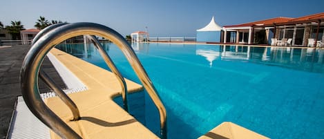 A clear blue pool with a metal ladder, a white umbrella, and a lounge area with white chairs.