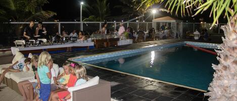 A poolside area with a dining setup and a seating area with children.