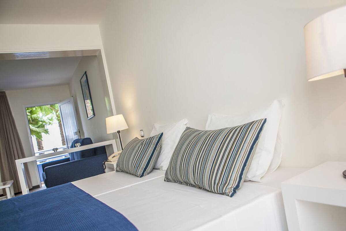 Ein Hotelzimmer mit Bett, Schreibtisch, Lampe und Blick ins Freie.