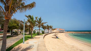 Una playa con cielo despejado, palmeras y un edificio de techo rojo.