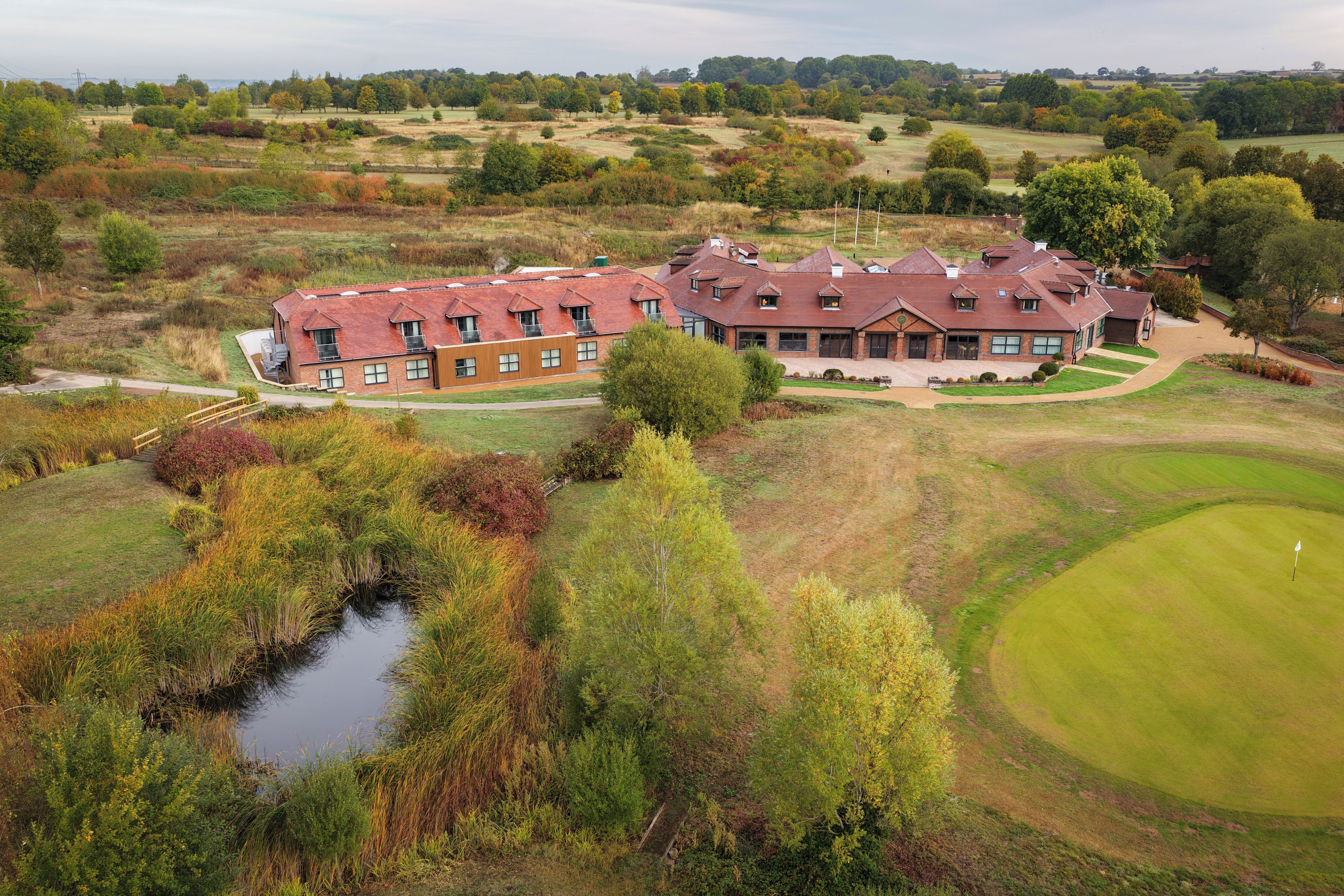 A large, multi-story building with a red-tiled roof, surrounded by a golf course and natural landscape.