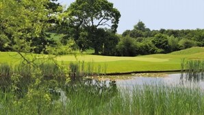 A golf course with a pond, trees, and a clear sky. - Bernwood Park Hotel (Aylesbury)