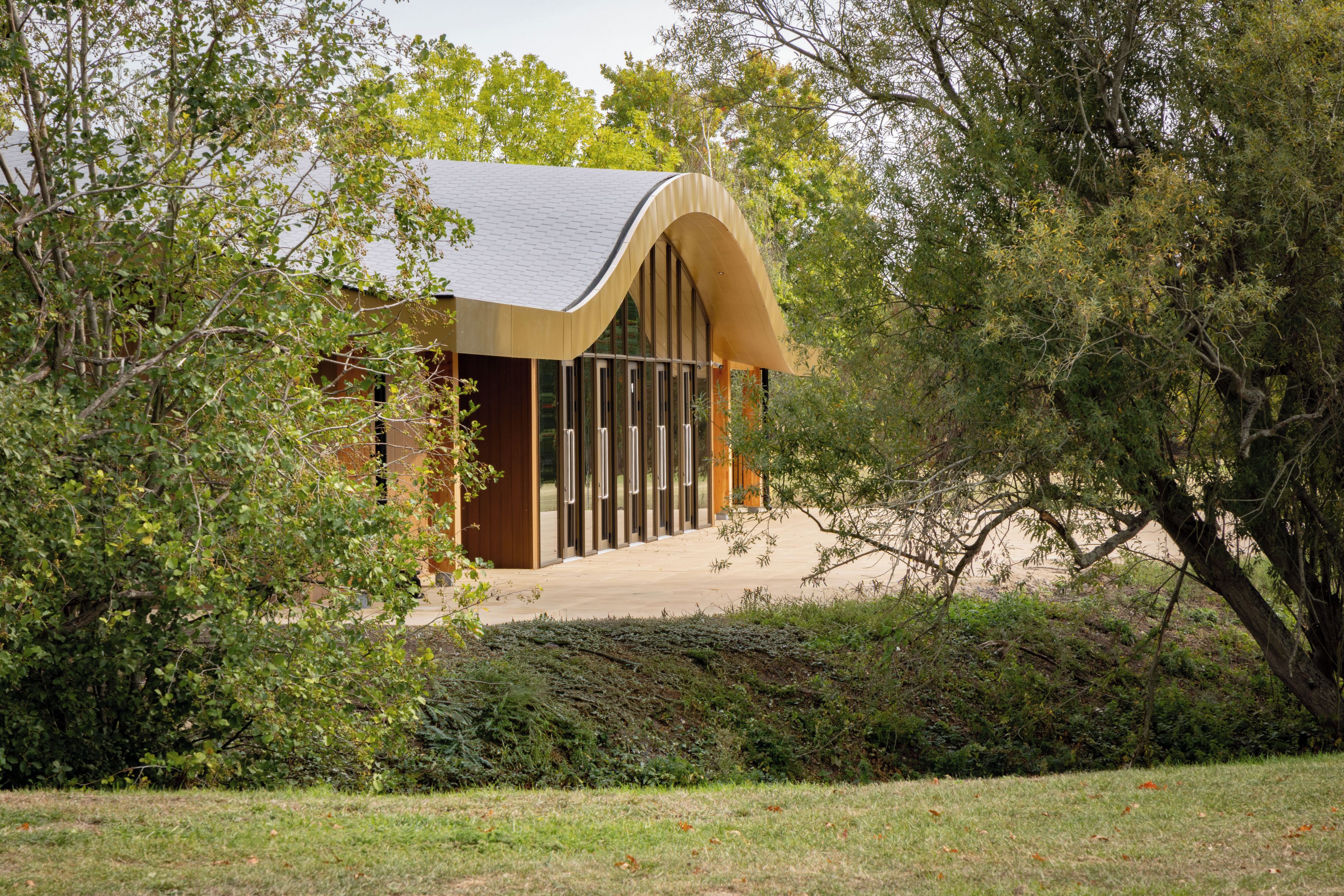 Un bâtiment moderne doté d’un toit incurvé, entouré d’une végétation luxuriante.