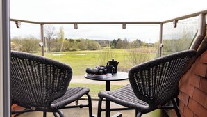 A balcony with two wicker chairs, a small table, and a view of a grassy field. - Bernwood Park Hotel (Aylesbury)