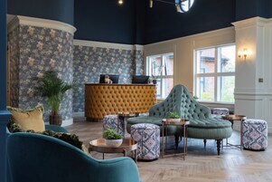 A lobby with a tufted sofa, patterned ottomans, a reception desk, and a large window.