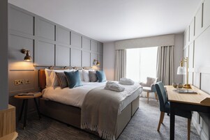 Una habitación de hotel moderna con una cama grande, mesitas de noche, un escritorio y una ventana con cortinas.