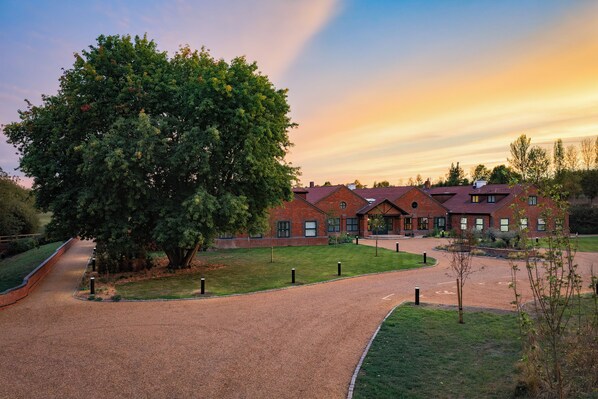 A brick building with a large tree in front, a gravel path, and a clear sky. - Bernwood Park Hotel (Aylesbury)