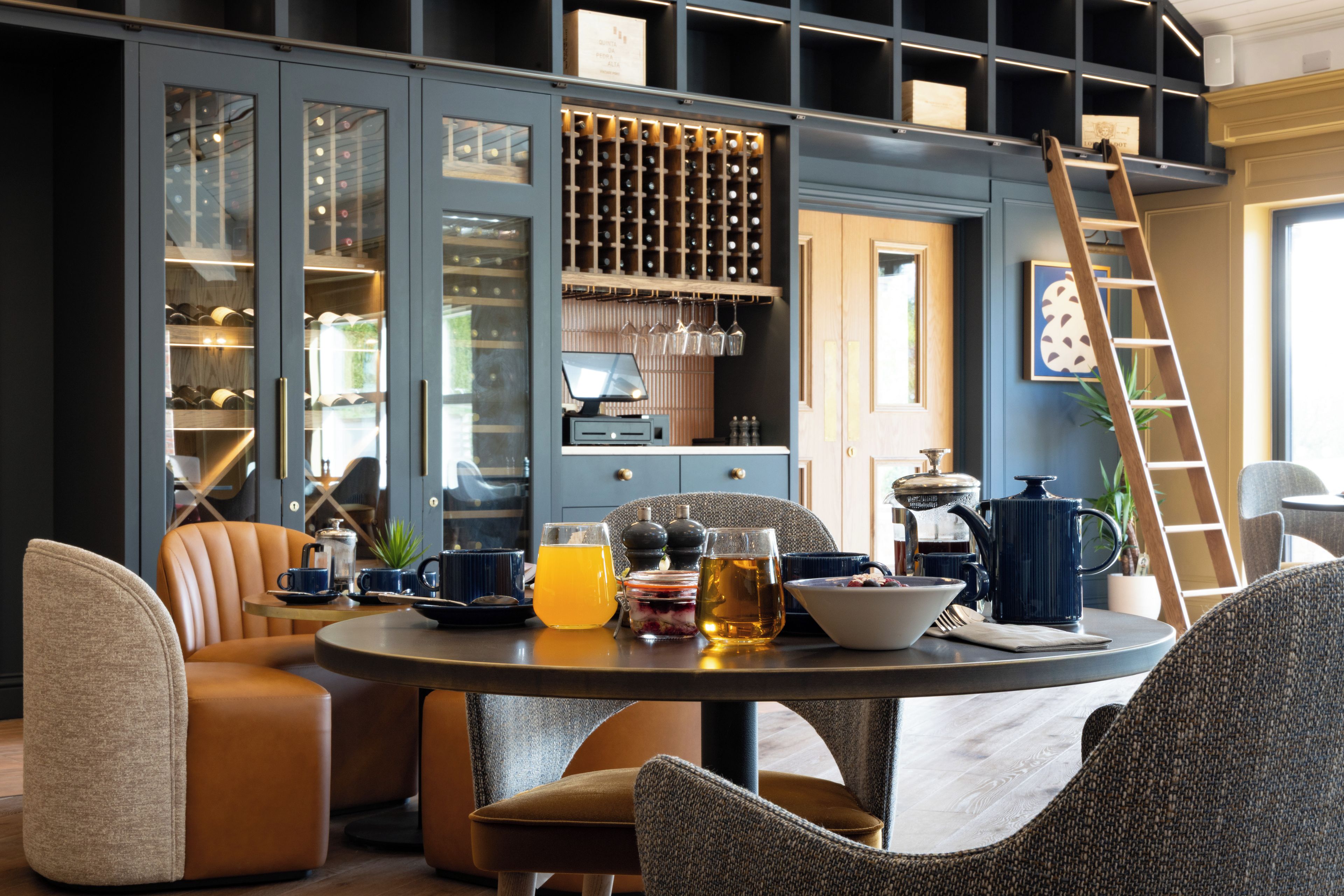 A modern dining area with a round table, leather chairs, and a wine rack in the background.