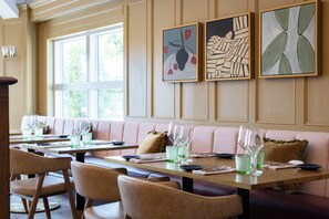 A restaurant interior with a long dining table, cushioned seating, and artwork on the walls. - Bernwood Park Hotel (Aylesbury)