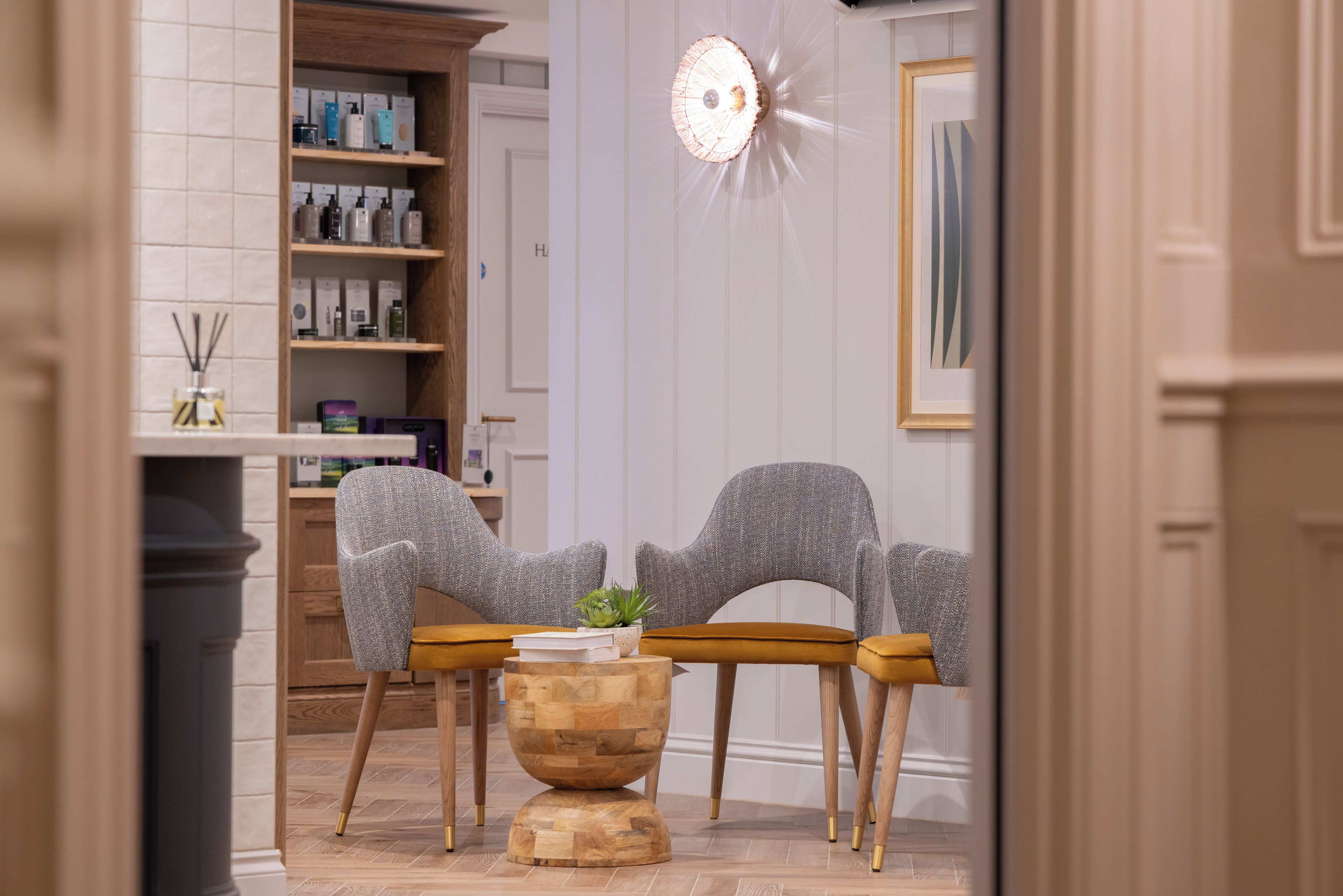 A salon with two grey chairs, a wooden table, and a mirror with a light fixture.