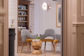 A salon with two grey chairs, a wooden table, and a mirror with a light fixture. - Bernwood Park Hotel (Aylesbury)