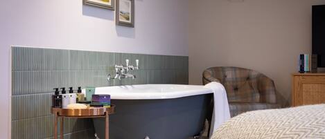 A bathroom with a bathtub, a vanity with toiletries, and a chair.