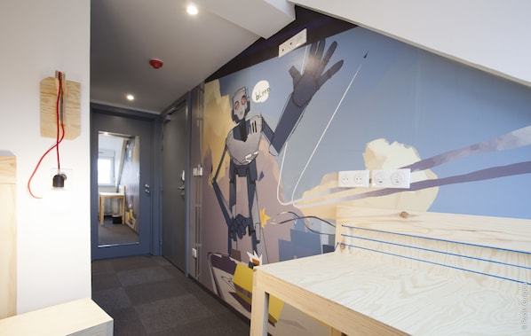Un pasillo con un mural de un robot, una mesa de madera y una puerta que da a otra habitación.
