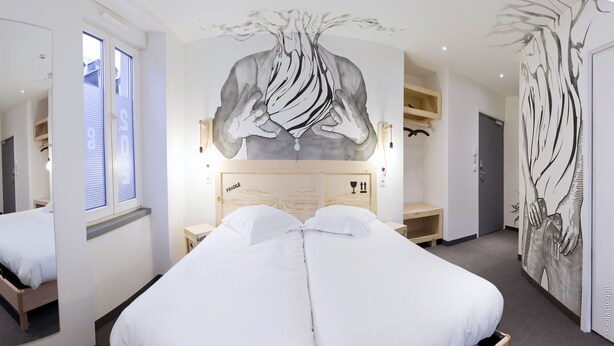 A modern hotel room with a large bed, a wooden headboard, and a wall mural. - Hotel Graffalgar (Strasbourg)