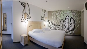 Een moderne hotelkamer met een groot bed, een hoofdbord met een houten structuur, en een muurschildering met abstracte handmotieven.