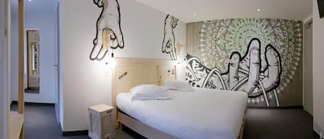Una habitación de hotel moderna con una cama grande, cabecera con textura de madera y un mural en la pared con diseños abstractos hechos a mano.