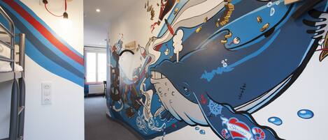 A hallway with a vibrant mural of a whale and various sea creatures, a staircase, and a radiator.