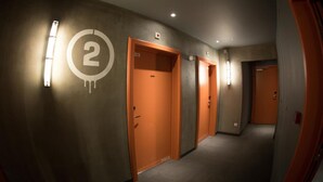 Een gang met genummerde deuren, inbouwspots en een tapijtvloer.