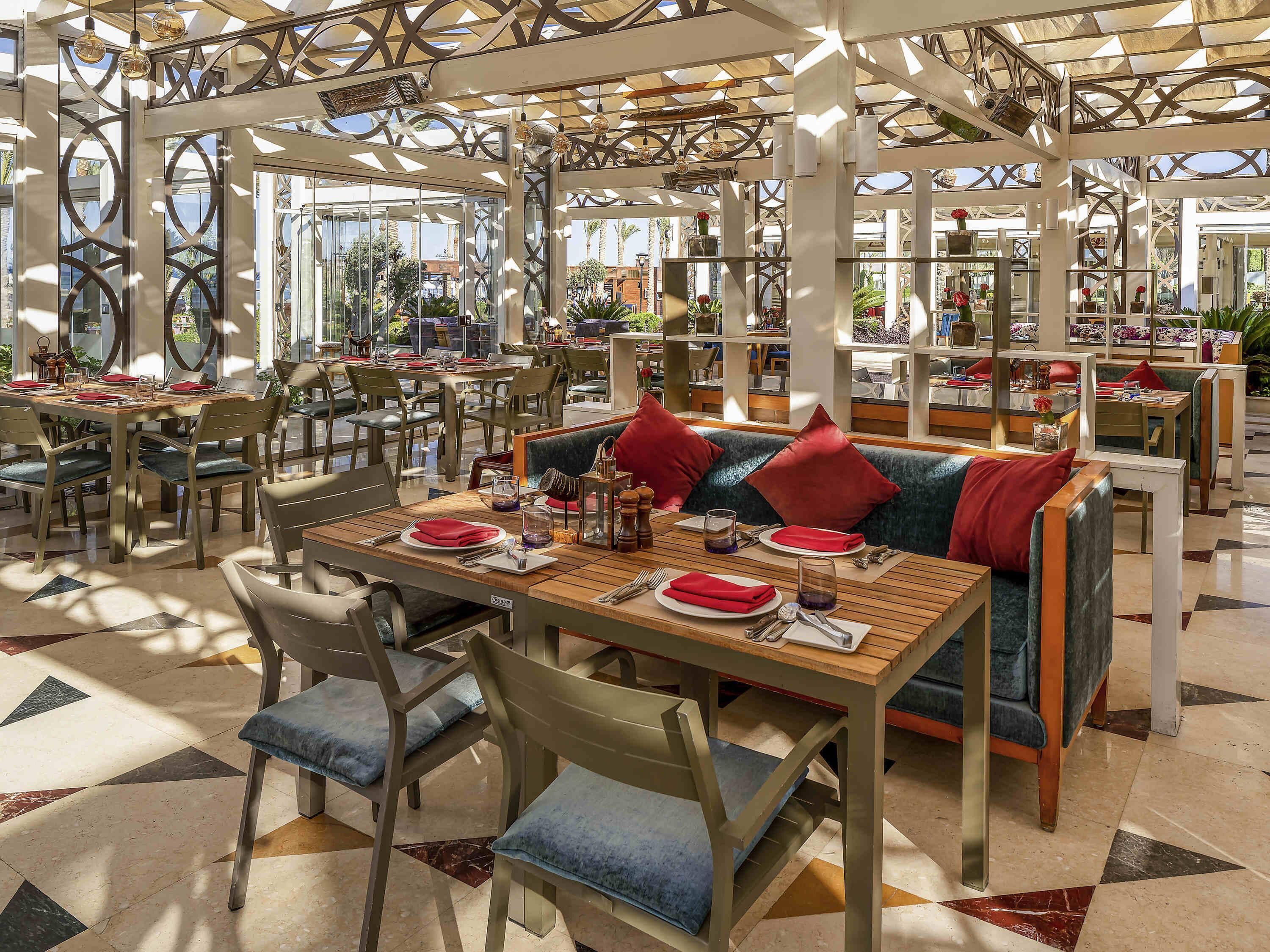 A spacious restaurant with multiple tables and chairs, a patterned floor, and a ceiling with geometric designs.