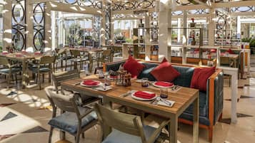 A spacious restaurant with multiple tables and chairs, a patterned floor, and a ceiling with geometric designs.