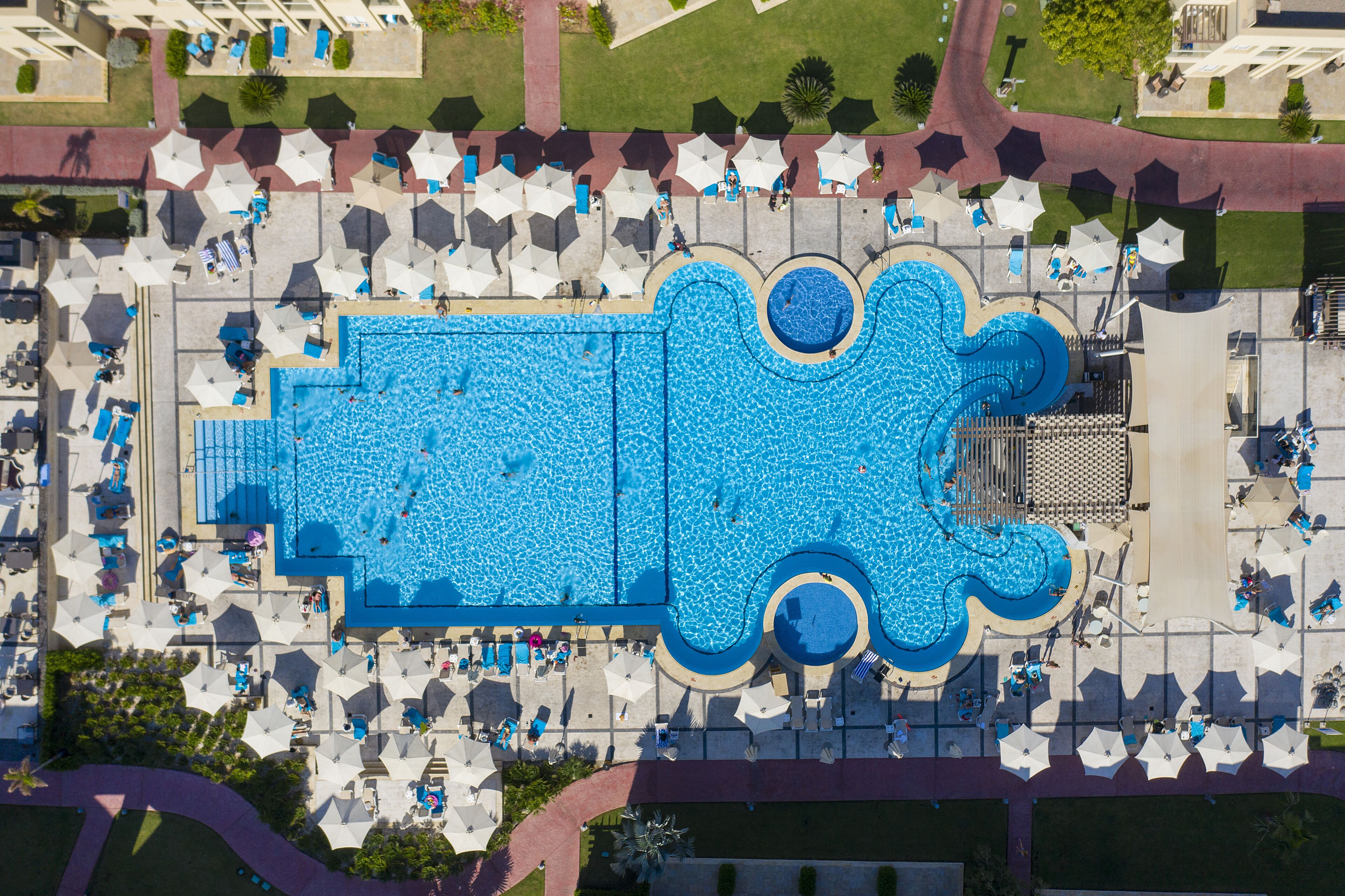 Luchtbeeld van een zwembadcomplex met meerdere zwembaden, ligbedden en parasols.