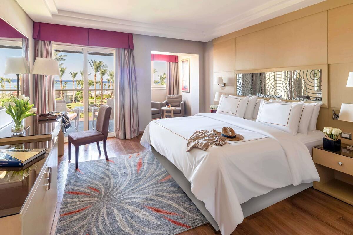 Habitación de hotel con cama, escritorio, silla, vista al mar y balcón.