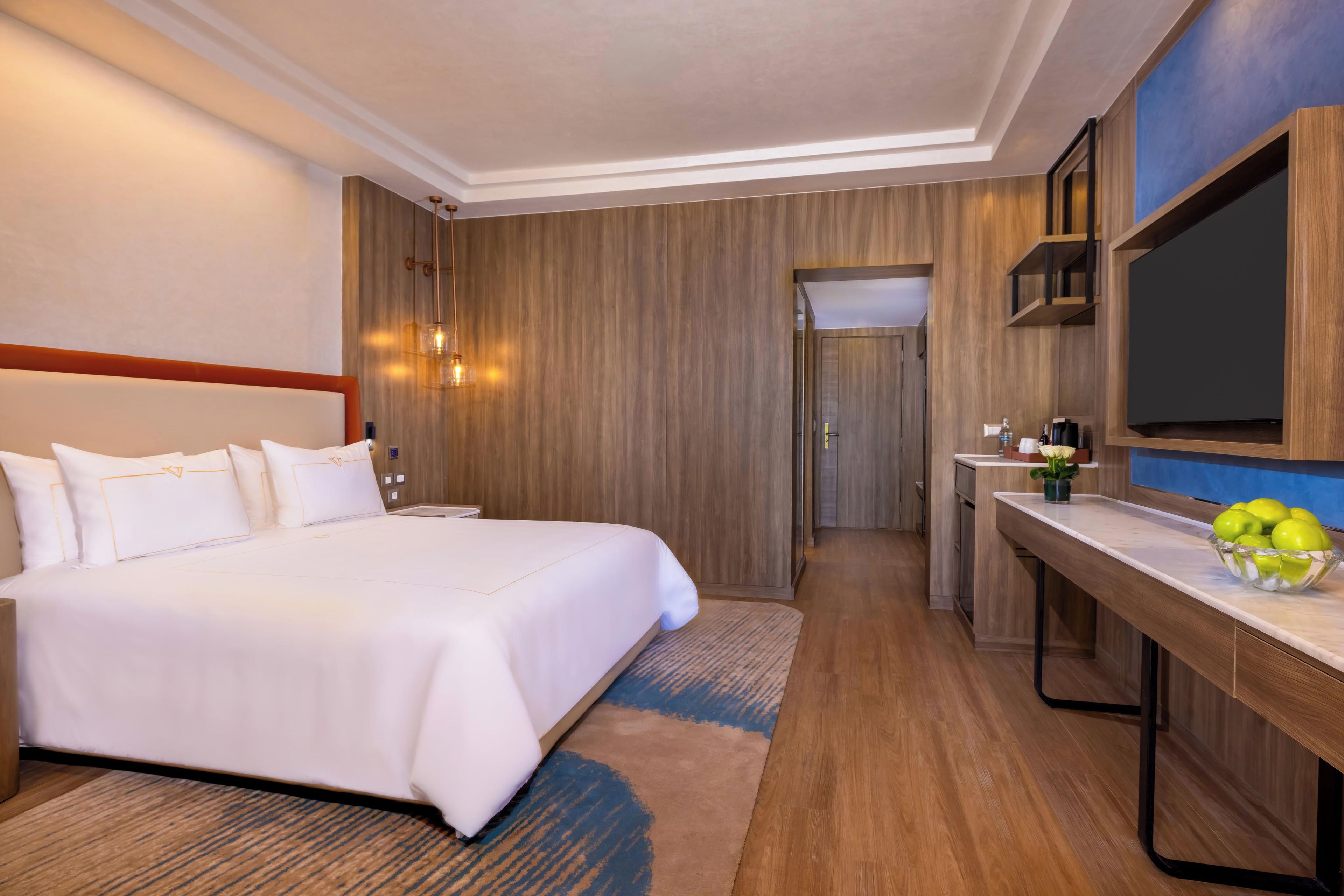 A hotel room with a large bed, a desk with a bowl of fruit, and a television on the wall.