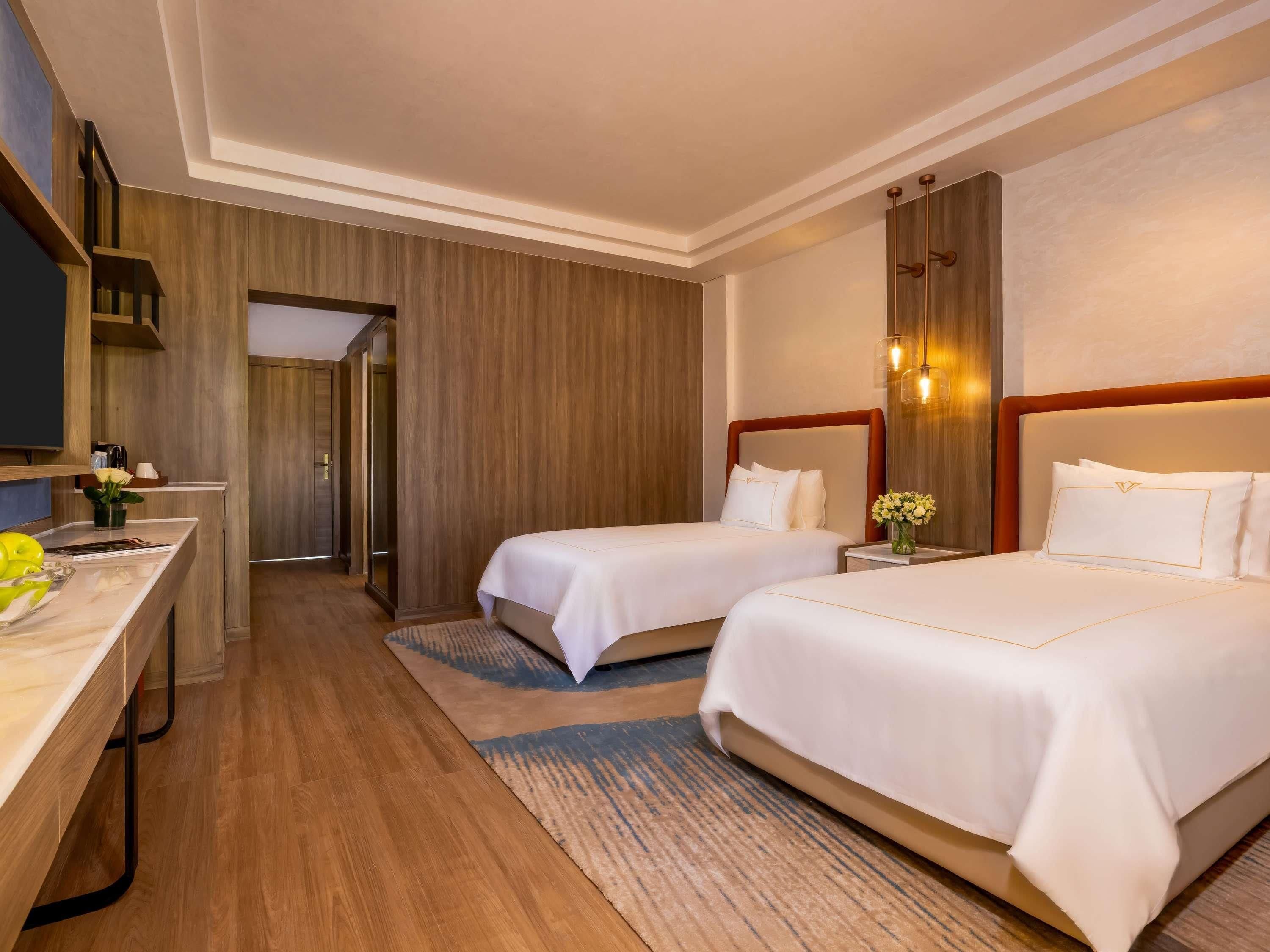 A hotel room with two beds, a desk, a television, and a bathroom visible through an open door.