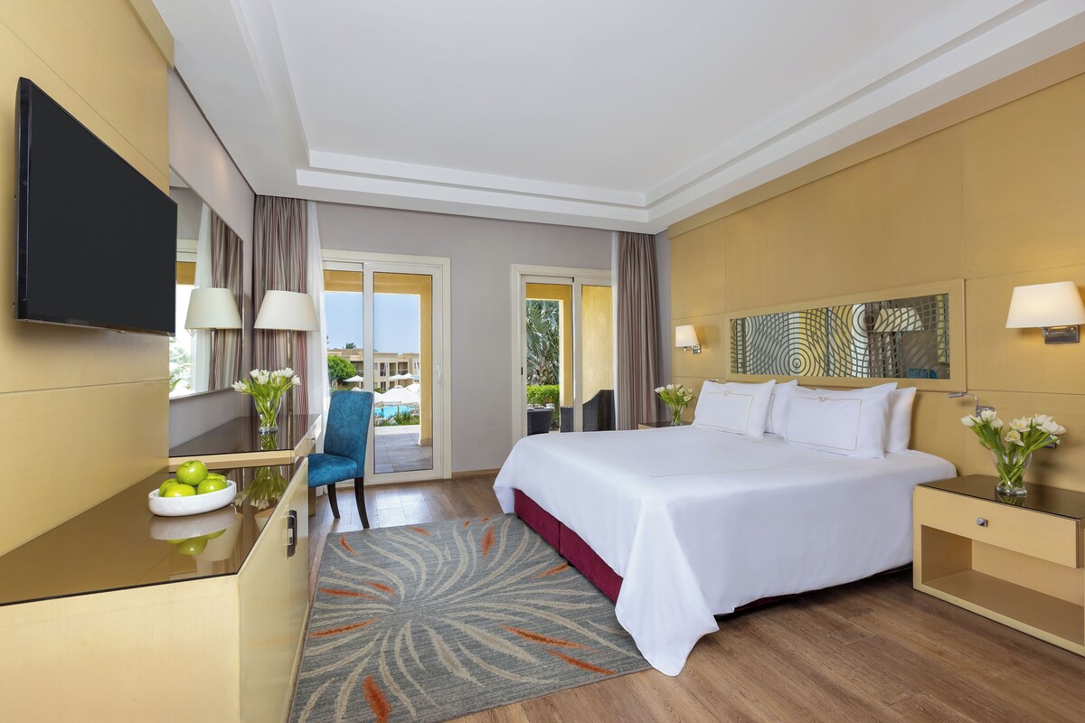 Habitación de hotel con cama, escritorio, silla, televisor y vistas al exterior.
