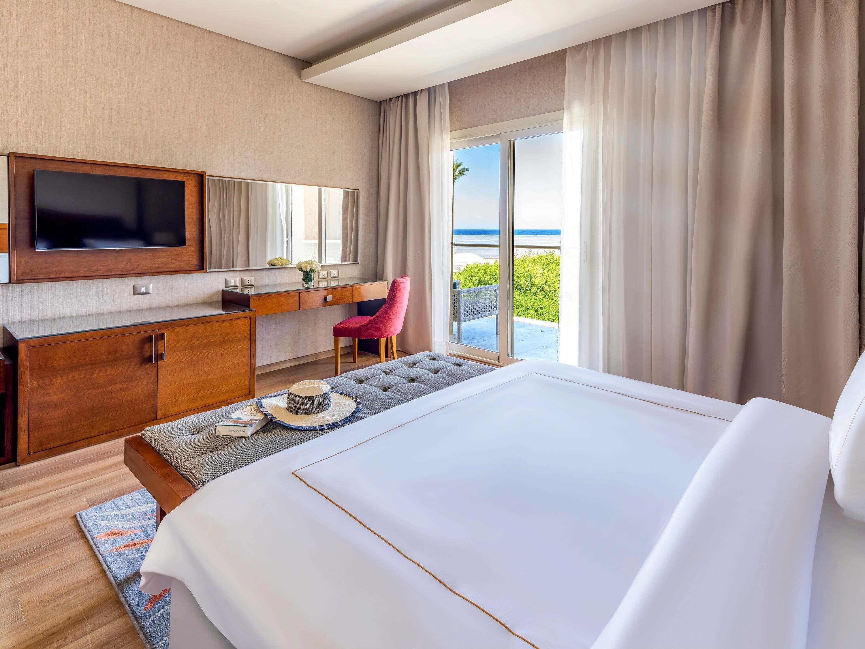 Een hotelkamer met een groot bed, een aan de muur bevestigde televisie, een bureau met stoel, en uitzicht op de oceaan.