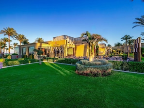 A modern hotel with a well-maintained lawn, palm trees, and outdoor seating areas.