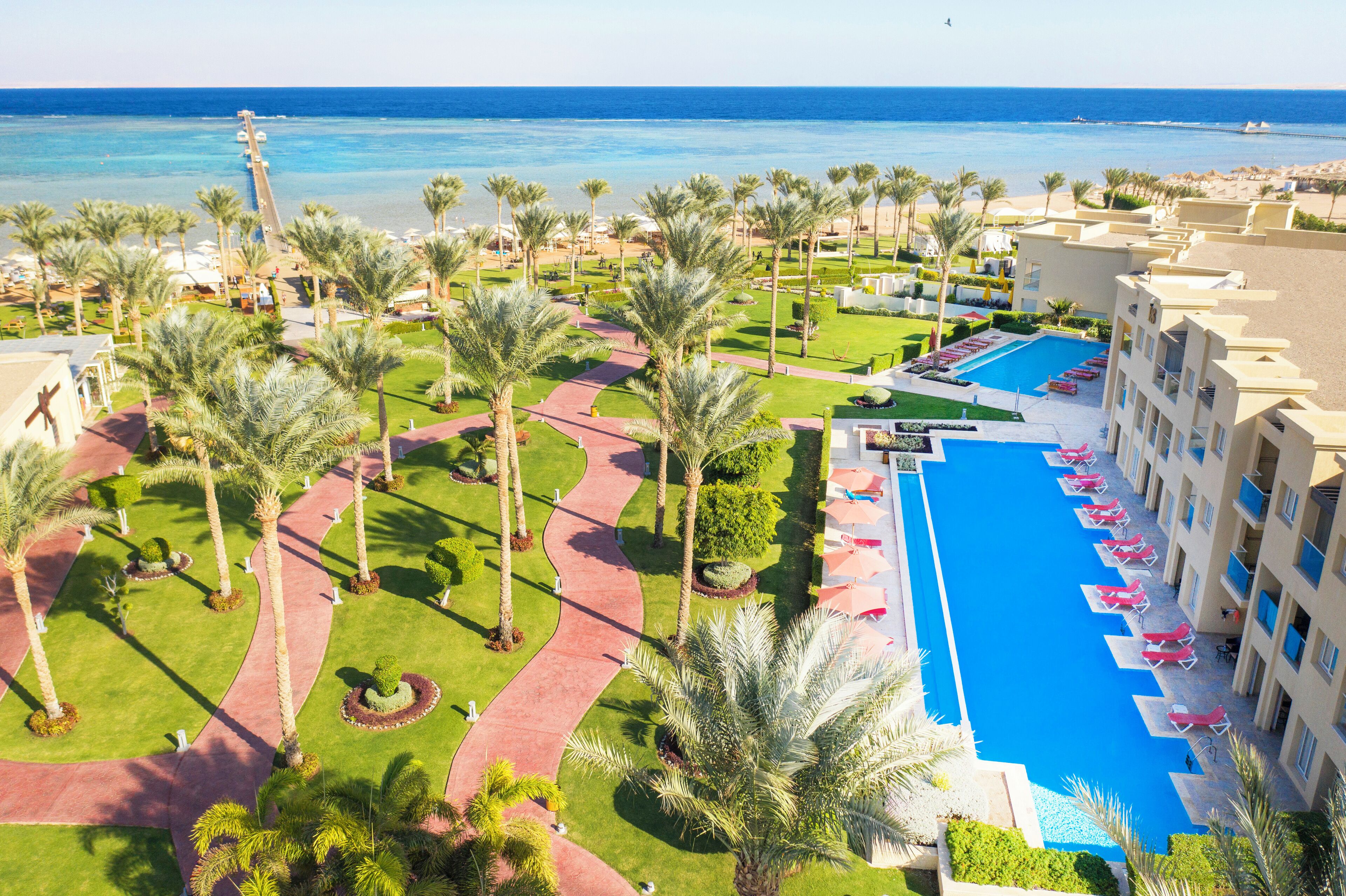 A resort with a swimming pool, palm trees, and a beach view.