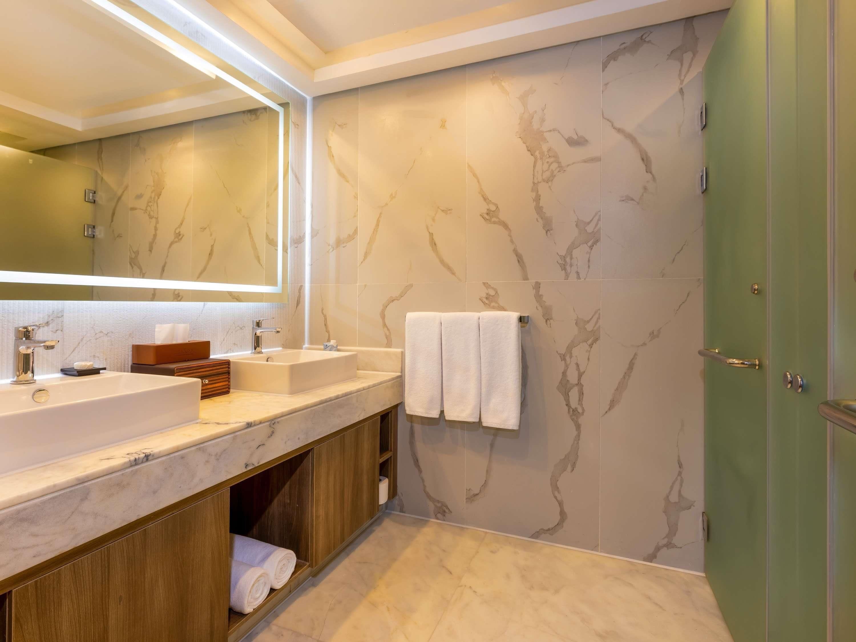 Une salle de bain avec un grand miroir, deux lavabos, un meuble-lavabo en bois et une porte verte.