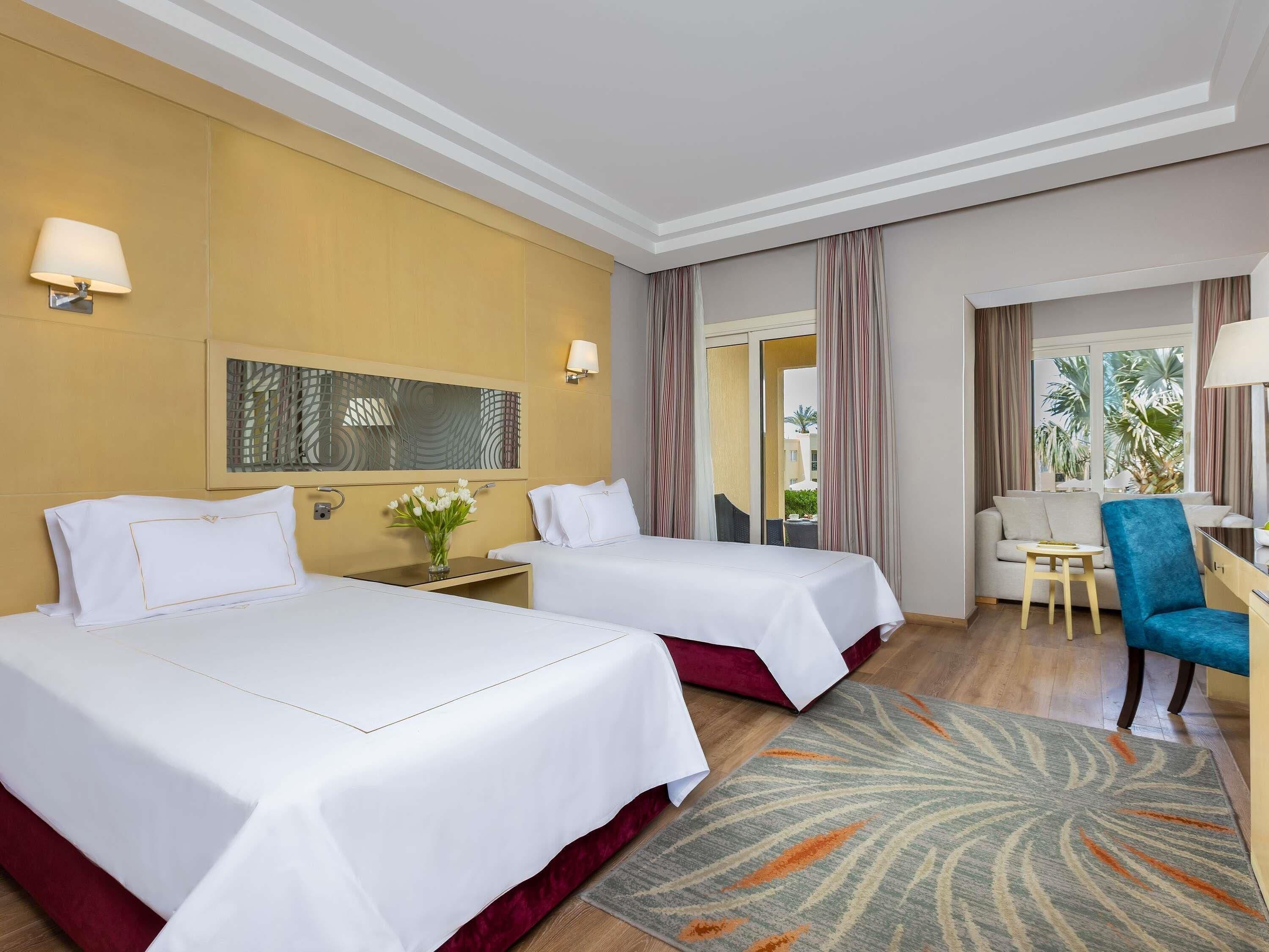 A hotel room with two beds, a sofa, a chair, a small table, and a view of the outdoors.