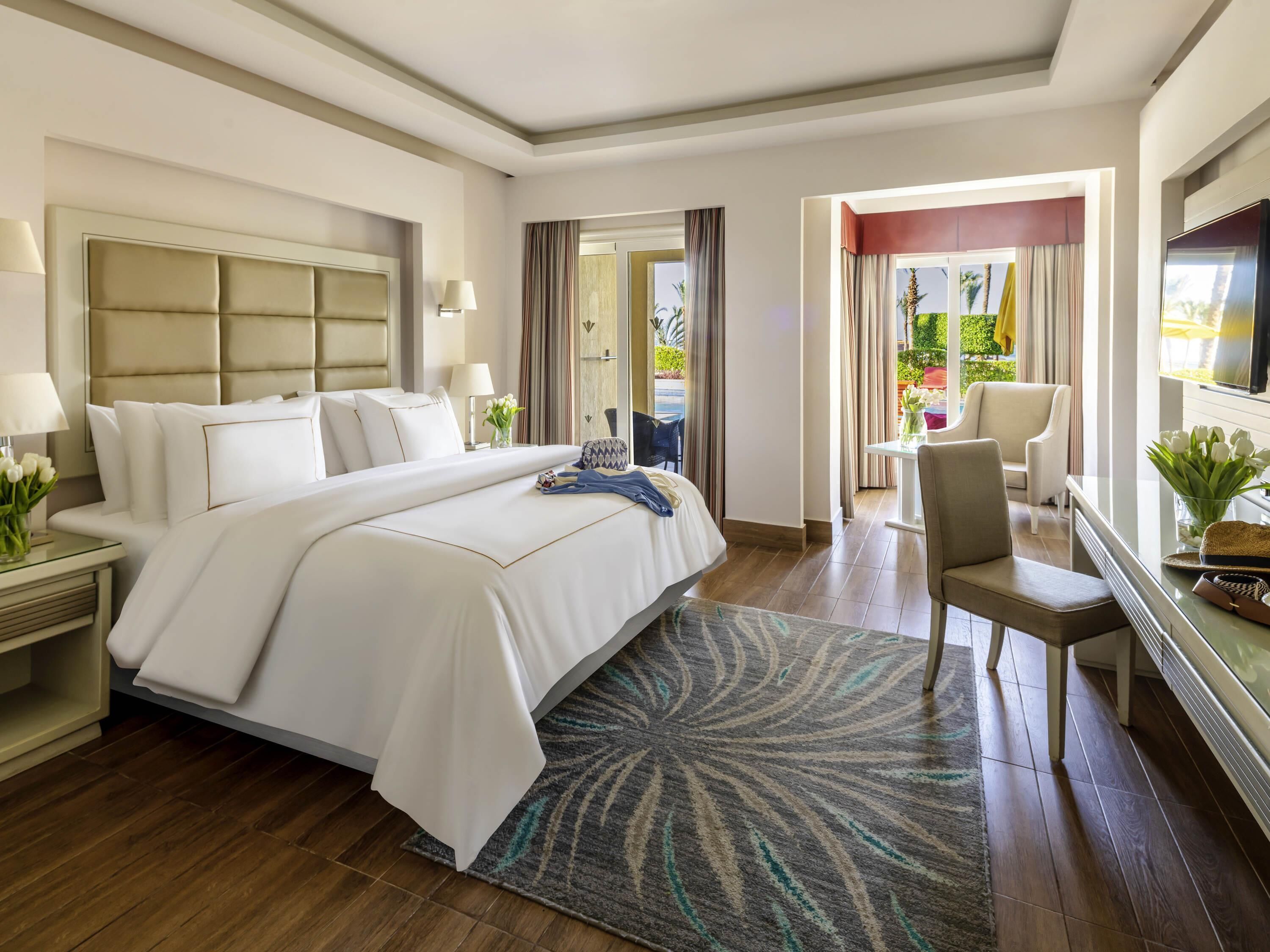 A hotel room with a large bed, a desk, a chair, a TV, and a view of the outdoors.