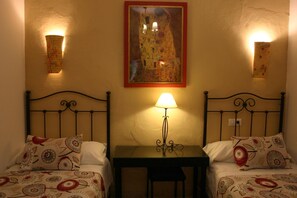 A room with two beds, a table, and a painting on the wall. - Pensión El Portillo (Córdoba)
