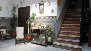 A traditional interior with a wooden chair, potted plants, a tiled wall with a decorative border, and a staircase. - Pensión El Portillo (Córdoba)