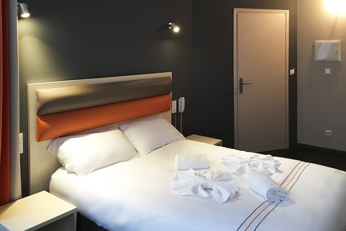 A hotel room with a bed, a nightstand, a door, and a wall-mounted phone.