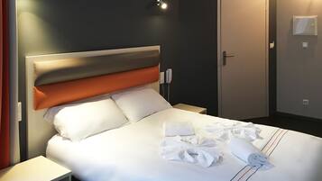 Een hotelkamer met een bed, een nachtkastje, een deur en een aan de muur bevestigd telefoon.