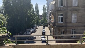 A balcony with white plastic chairs and a white ottoman, overlooking a street with parked cars and buildings. - Adonis Hotel Strasbourg (Strasbourg)