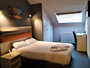 A modern hotel room with a neatly made bed, a desk with a chair, a radiator, and a skylight. - Adonis Hotel Strasbourg (Strasbourg)