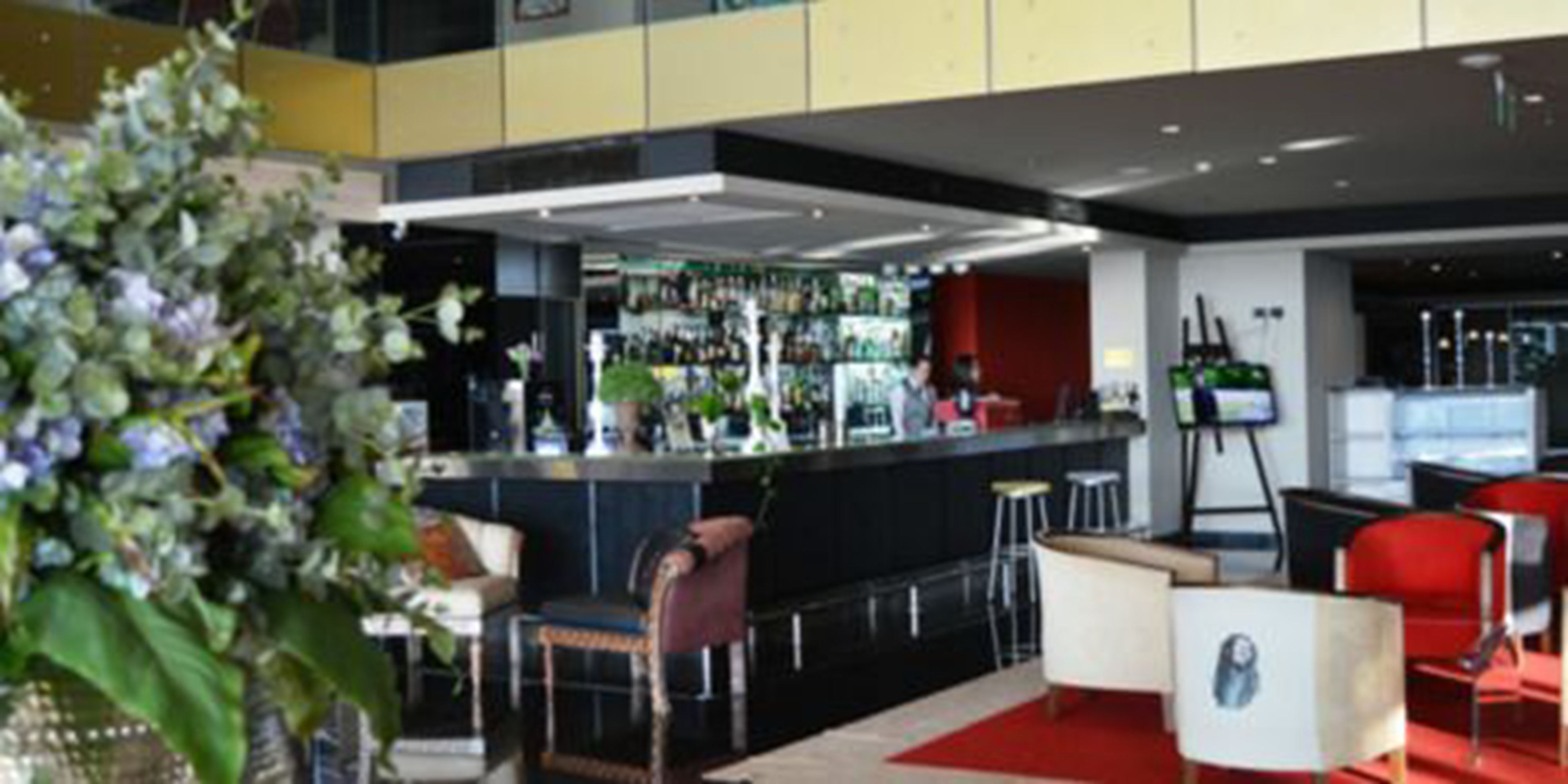 A modern bar area with a counter, stools, and a seating area with red chairs.