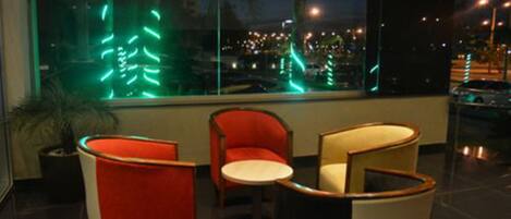 Un interior moderno con dos sillones rojos y una mesita, y un ventanal con vista a un paisaje urbano nocturno.