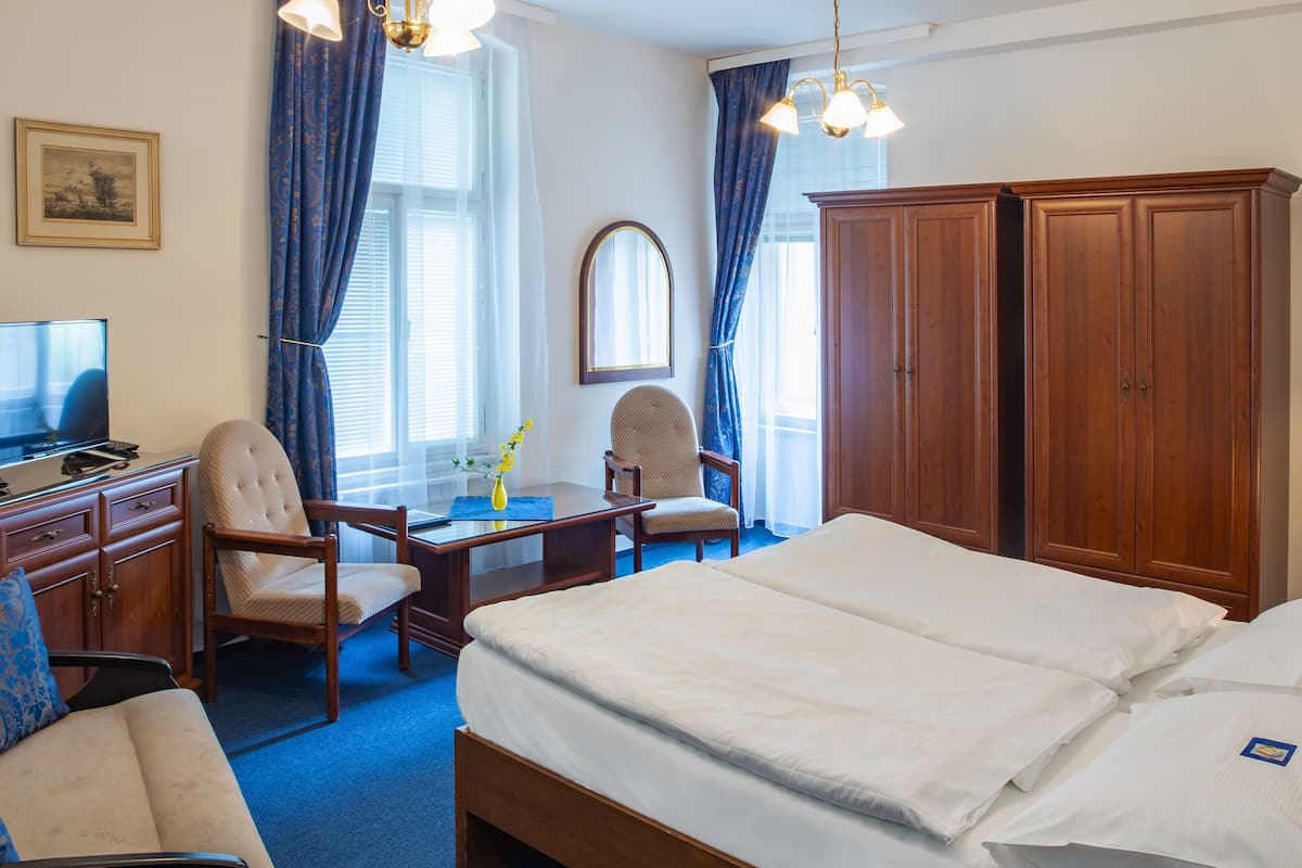 Habitación de hotel con cama, escritorio con ordenador, dos sillas, armario y ventana con cortinas.