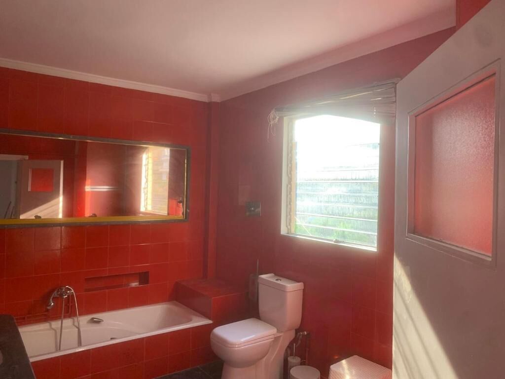 A bathroom with red walls, a white bathtub, a white toilet, and a window with blinds.