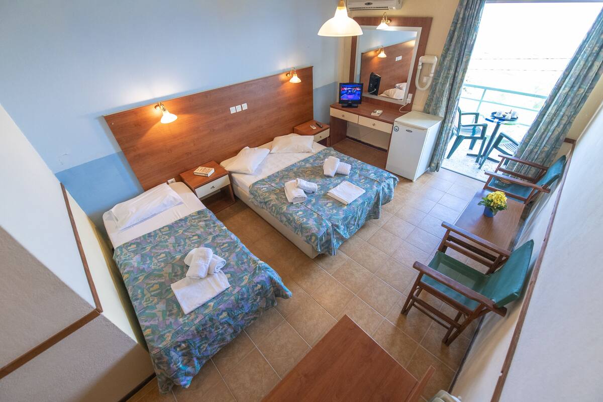 A hotel room with two beds, a desk, a chair, and a small kitchenette.