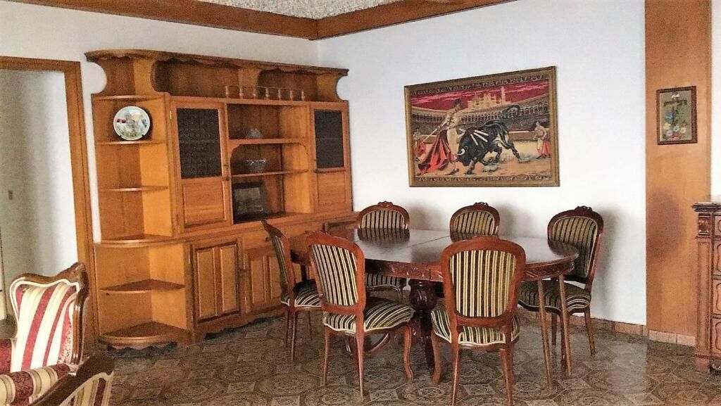Een eetruimte met een houten kast, een ronde tafel en zes gestreepte stoelen.