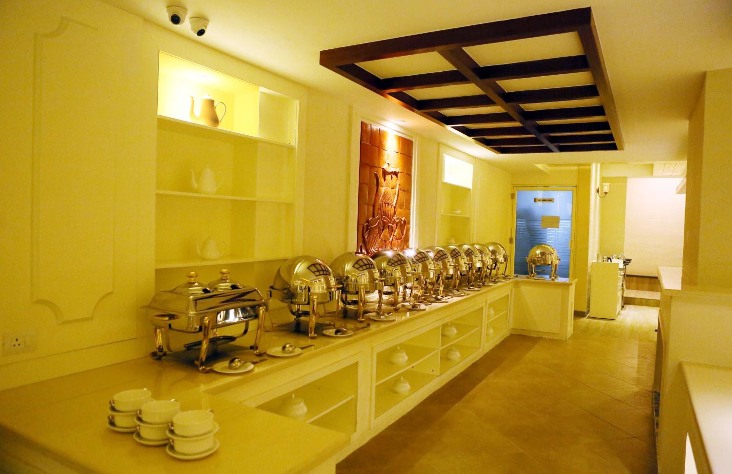 A hotel kitchen with a long buffet counter, stainless steel appliances, and a decorative wall piece.